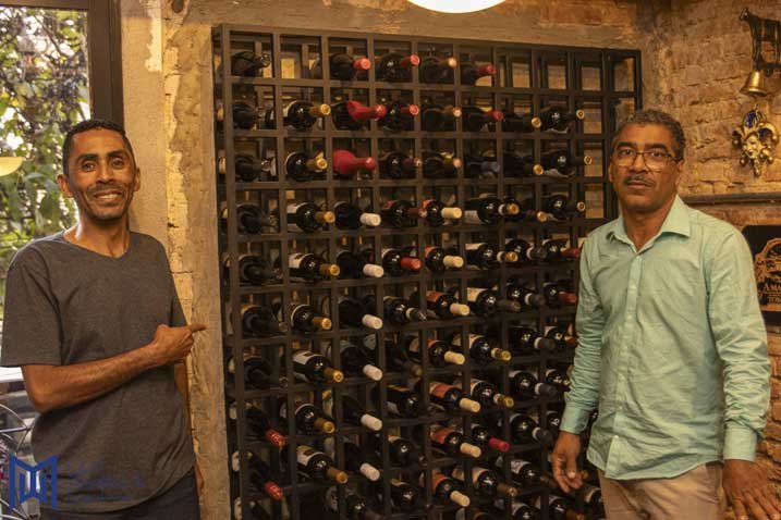dois homens parados ao lado de uma prateleira com garrafas de vinho
